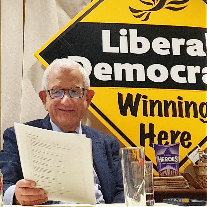 Photo of Jeffrey Gruder, Chair of the Hertsmere Lib Dems, smiling in front of a "Liberal Democrats Winning Here" banner.